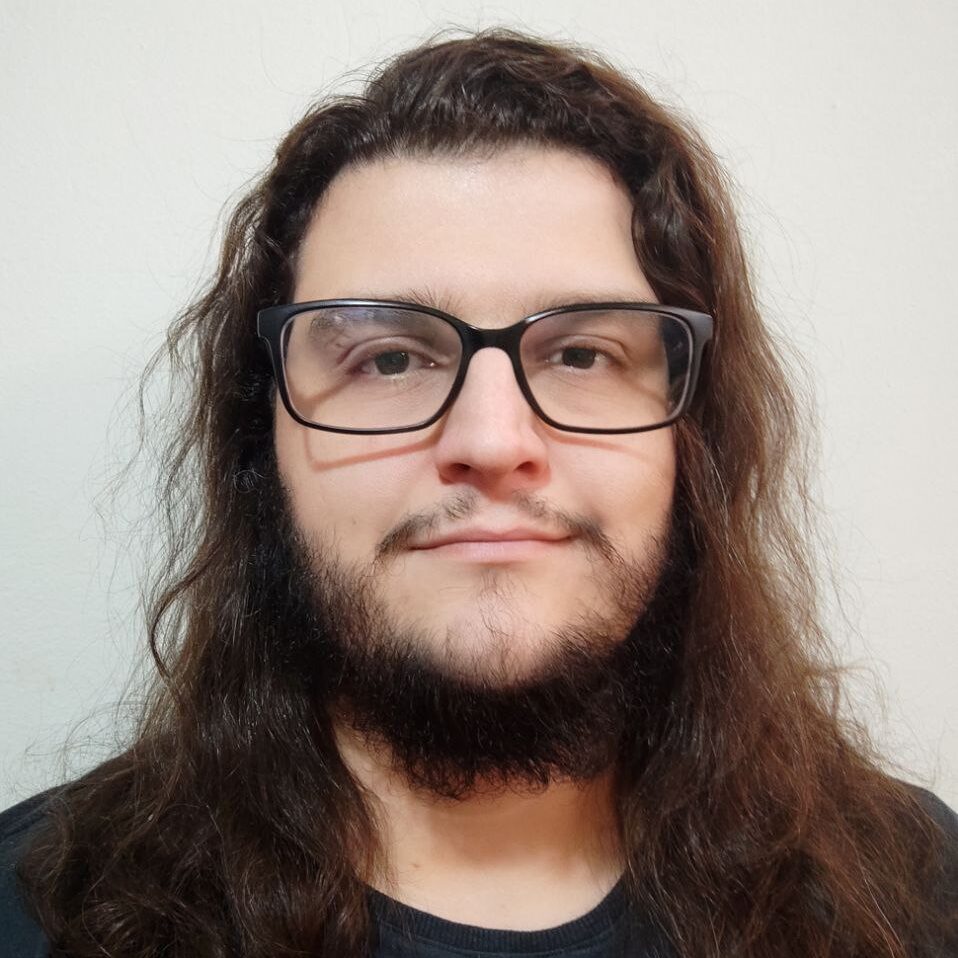 Foto do autor. Homem branco, cabelos castanhos compridos e barba. Usando óculos de armação preta e camiseta preta.